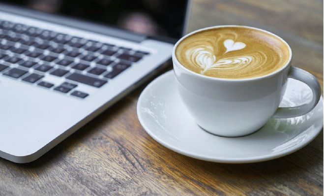 Dator och en kopp kaffe med latte art, symbol för ett digitalt lunchwebbinarium